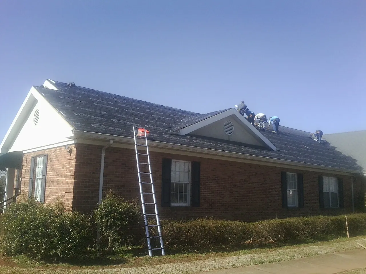 Crew tearing shingles off a brick ranch roof with a ladder set — Emergency Roof Repair work by our crew in Athens