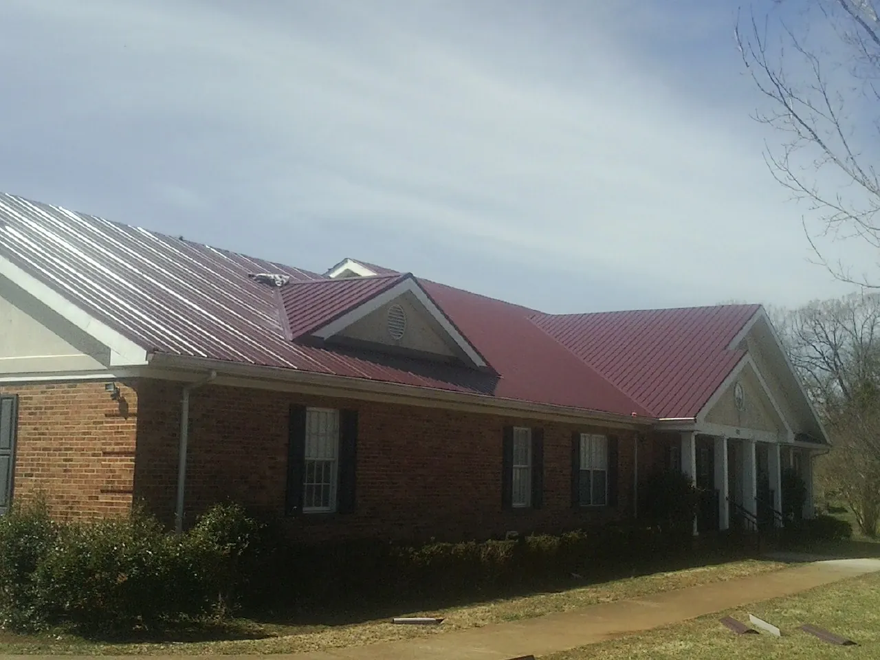 Red metal roof with gabled entries on a long brick building, from a Hail Damage Roof Repair job in Athens