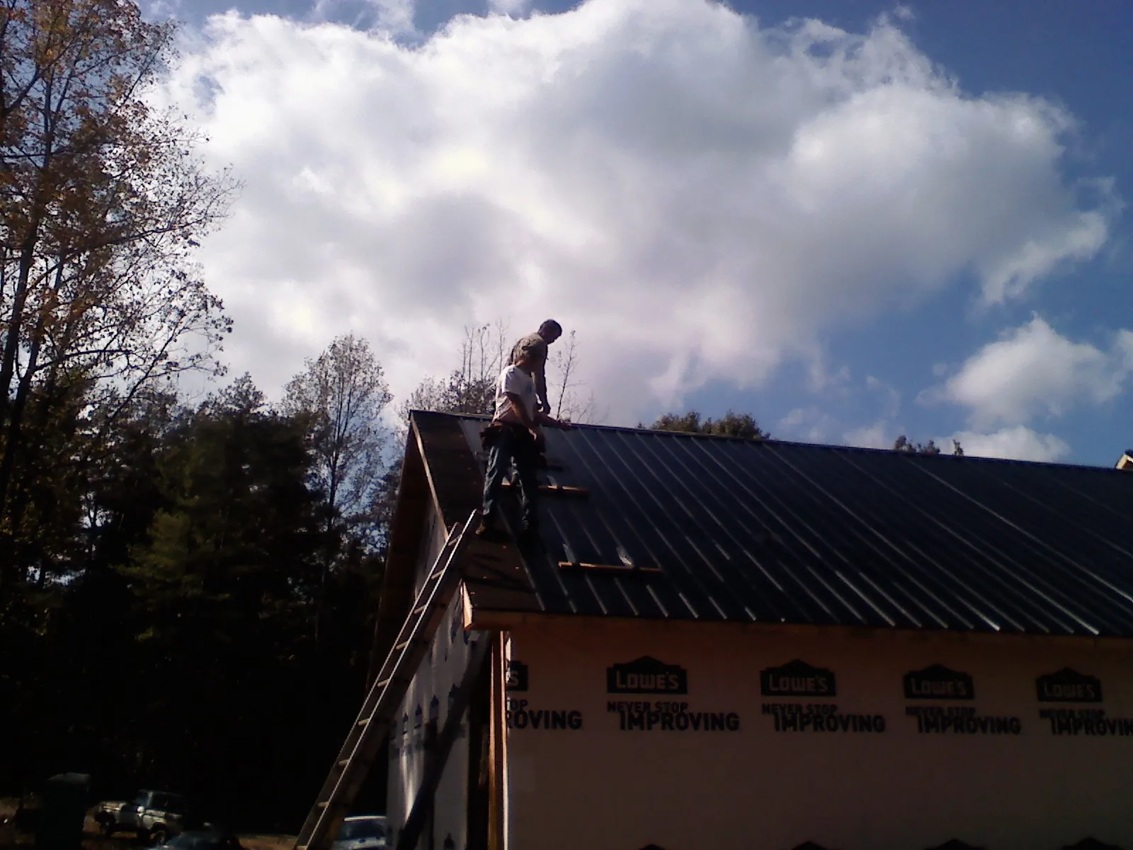Roofer fastening dark metal panels high against a cloudy sky, from a Roof Inspection job in Athens